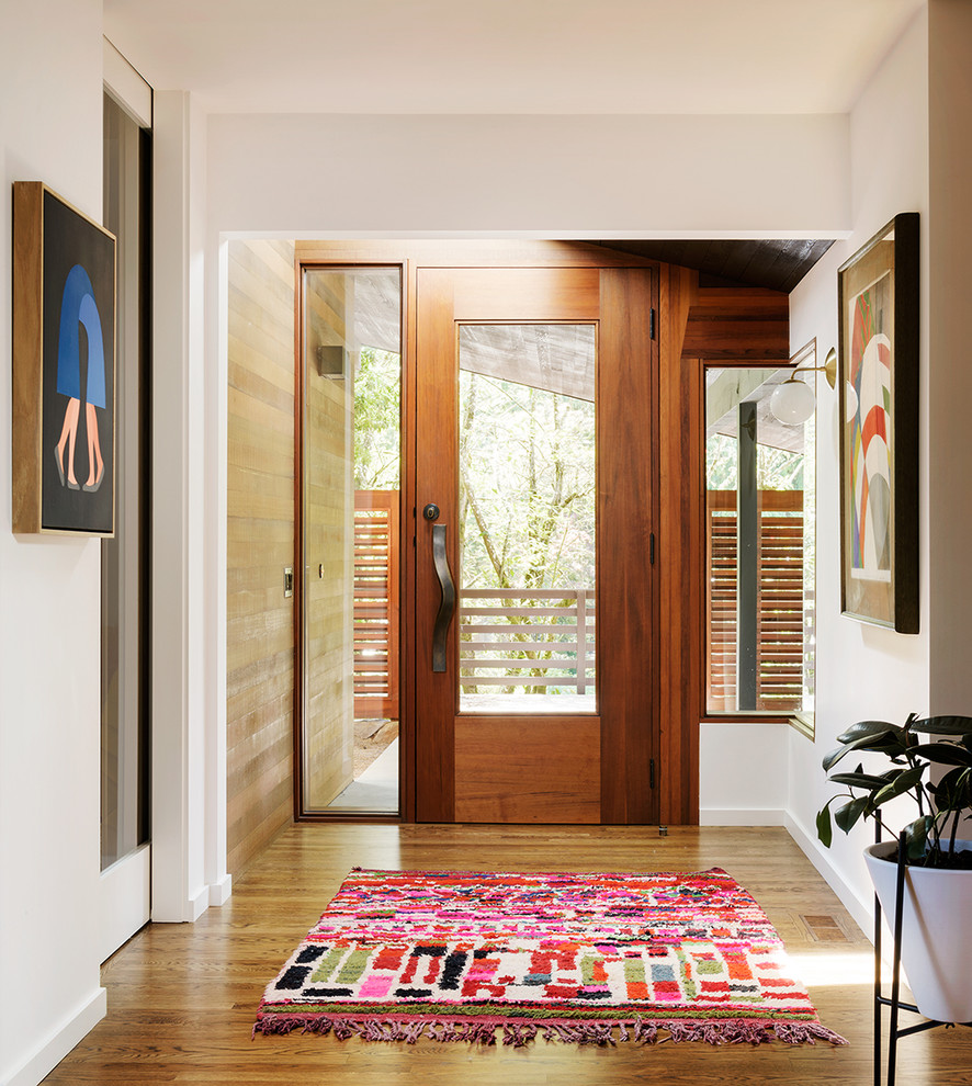 Cette image montre une entrée vintage avec un couloir, un mur blanc, un sol en bois brun, une porte simple et une porte en verre.