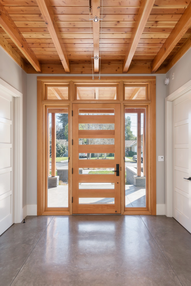 Réalisation d'une entrée chalet avec sol en béton ciré, une porte simple et une porte en bois clair.