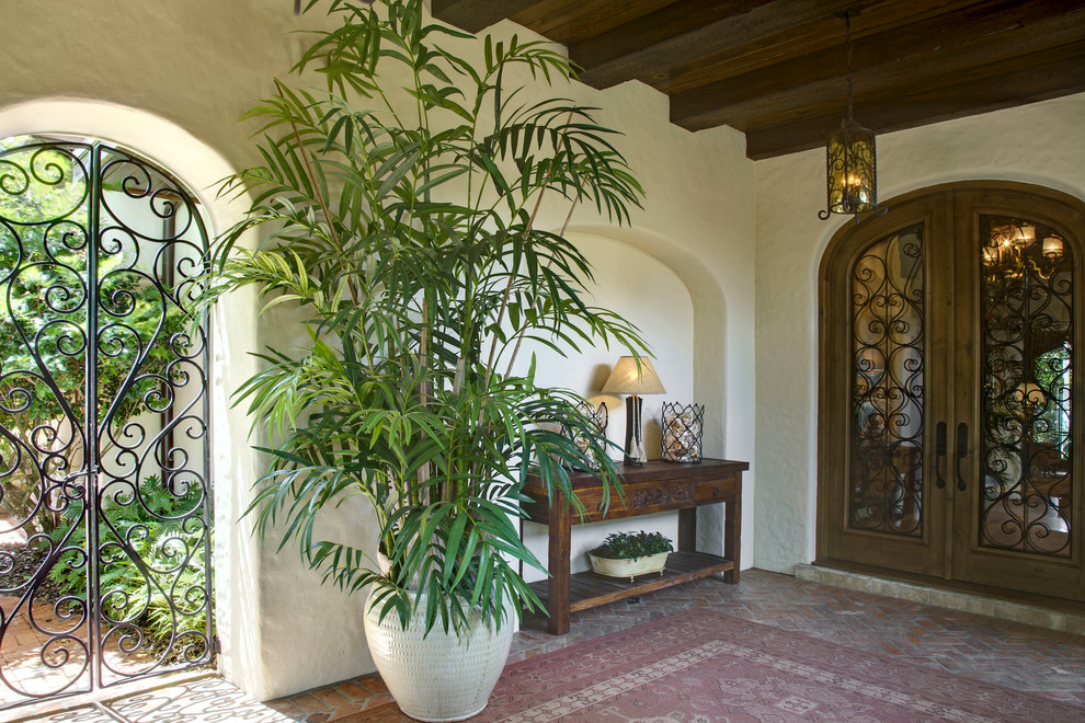 Пример оригинального дизайна: большая входная дверь в средиземноморском стиле с белыми стенами, кирпичным полом, двустворчатой входной дверью и входной дверью из темного дерева