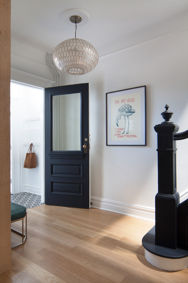 Aménagement d'un vestibule classique avec un mur blanc, parquet clair, une porte simple, une porte noire et un sol marron.