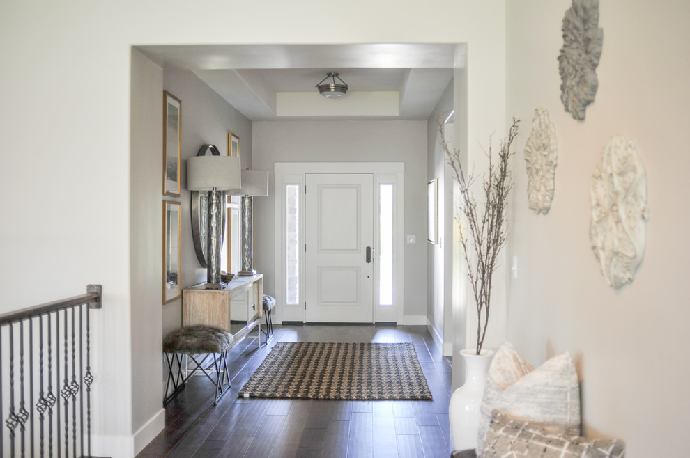 Aménagement d'un grand hall d'entrée classique avec un mur gris, parquet foncé, une porte simple, une porte blanche et un sol marron.