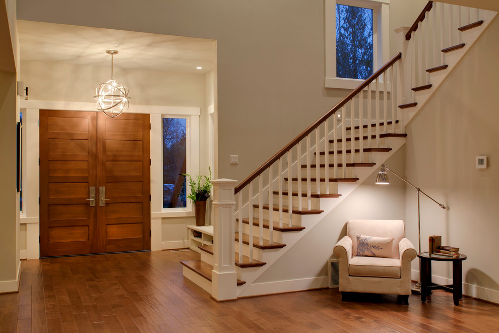 Cette image montre un grand hall d'entrée design avec un mur gris, un sol en bois brun, une porte double et une porte en bois brun.