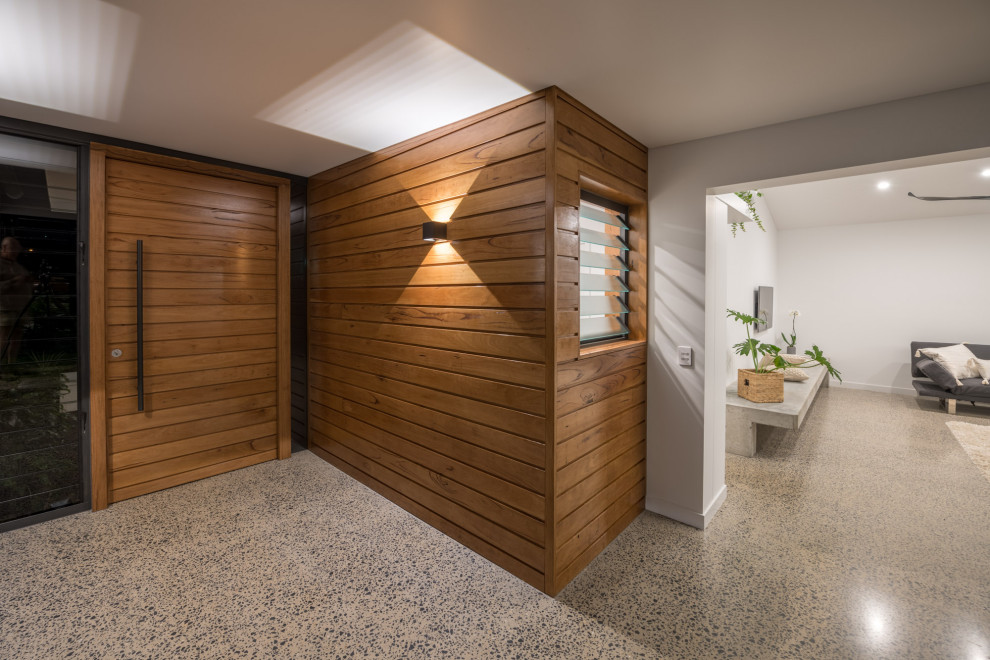 Réalisation d'une porte d'entrée minimaliste de taille moyenne avec un mur gris, sol en béton ciré, une porte pivot, une porte en bois brun, un sol gris et du lambris de bois.