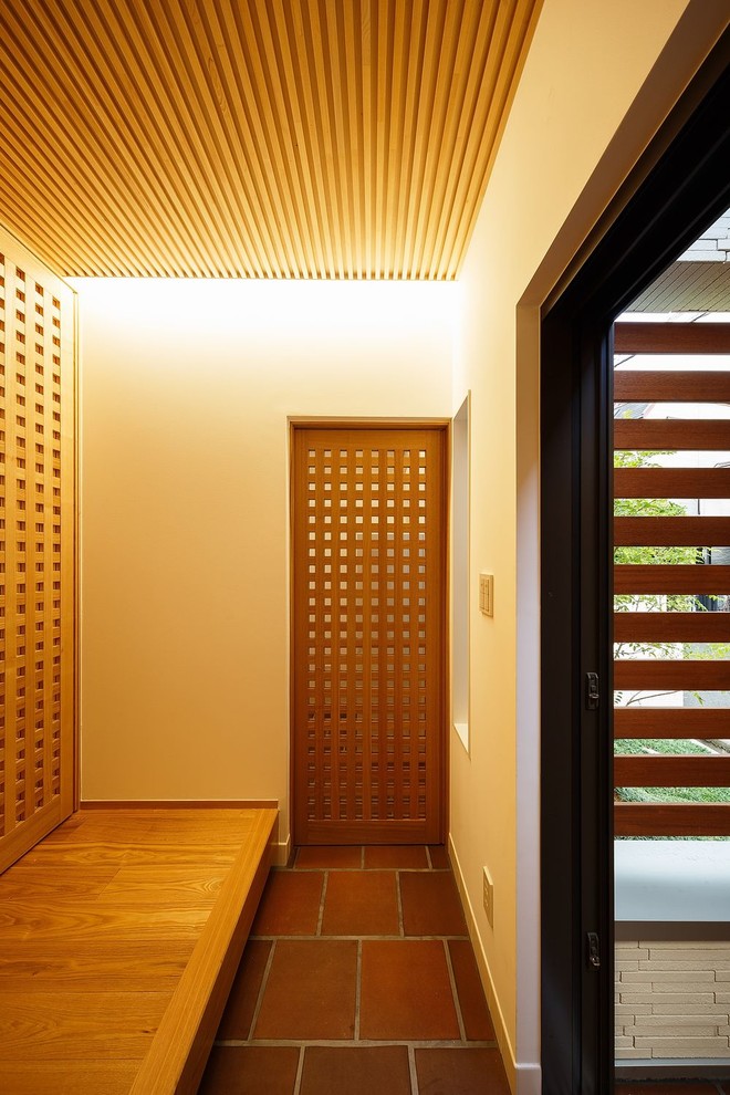 Exemple d'une entrée moderne de taille moyenne avec tomettes au sol, une porte simple, un couloir, un mur blanc, une porte marron et un sol marron.