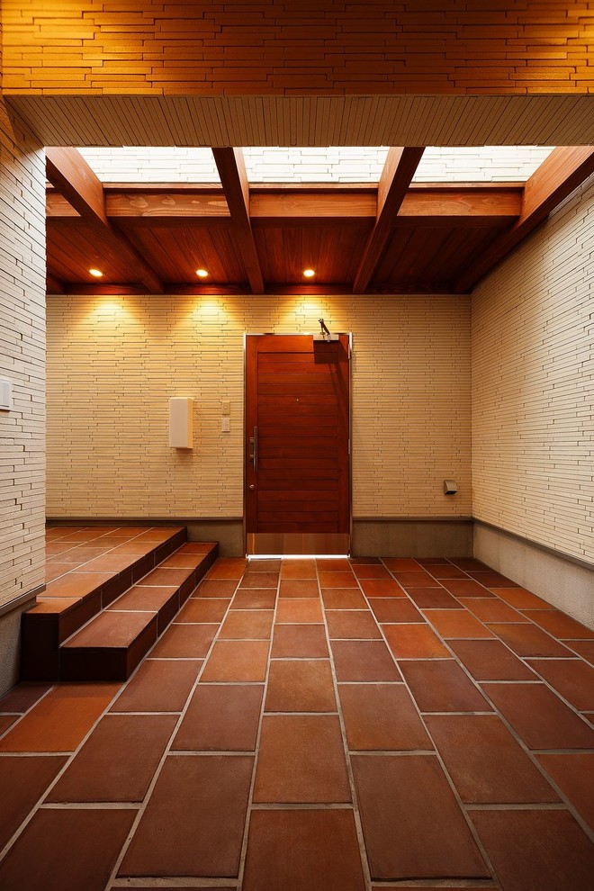 Cette image montre une grande entrée minimaliste avec tomettes au sol, une porte simple, une porte en bois brun, un couloir, un mur blanc, un sol marron et un plafond en bois.