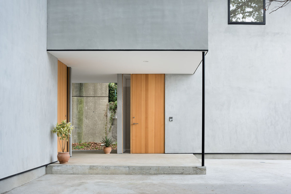 Réalisation d'une porte d'entrée design avec une porte simple, une porte en bois clair, un mur gris, sol en béton ciré et un sol gris.