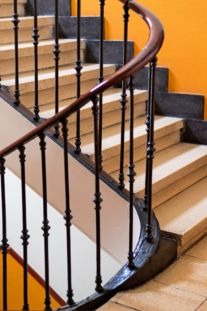 Imagen de escalera curva clásica grande con escalones de mármol, contrahuellas de mármol y barandilla de madera