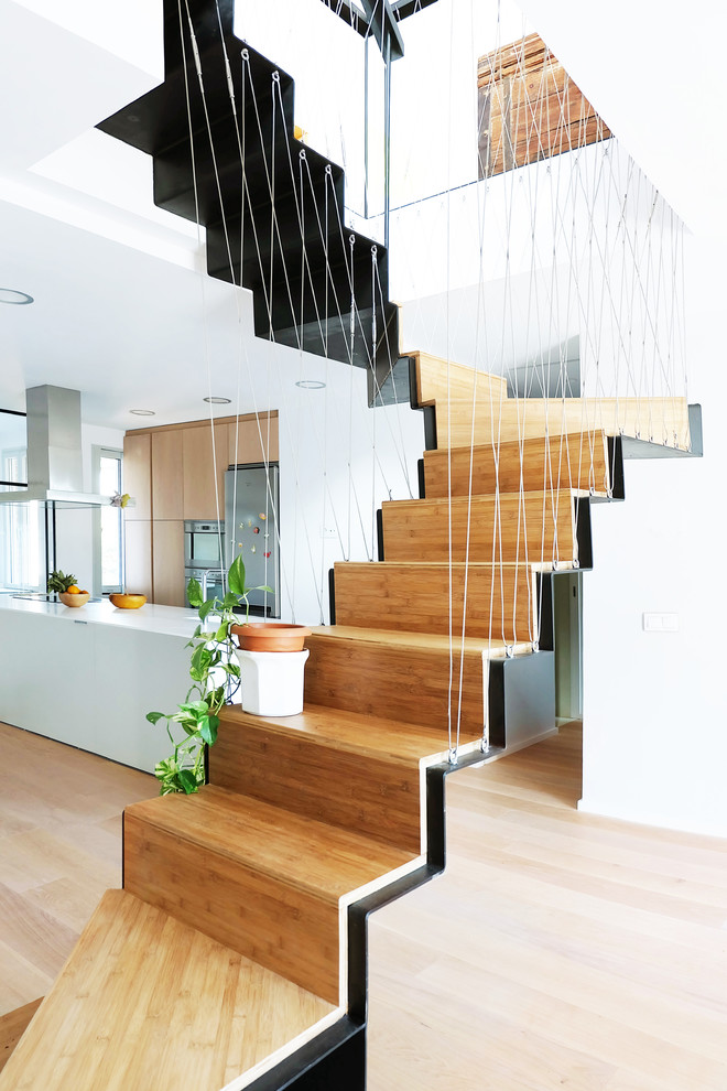 Aménagement d'un escalier courbe contemporain avec des marches en bois, des contremarches en bois et un garde-corps en câble.