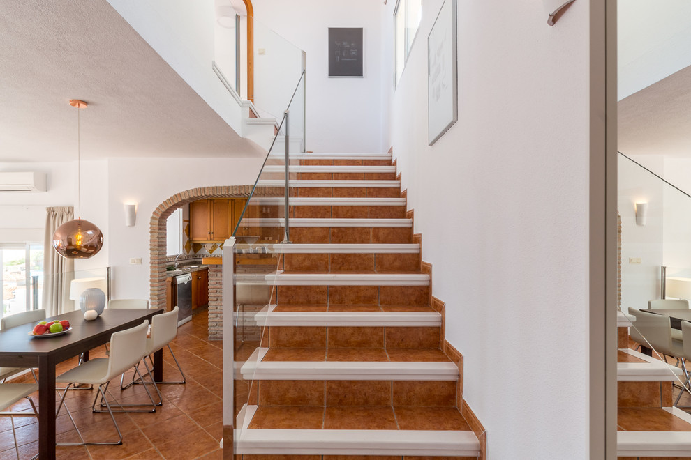 Cette photo montre un petit escalier méditerranéen en L avec des marches en terre cuite, des contremarches en terre cuite et un garde-corps en verre.