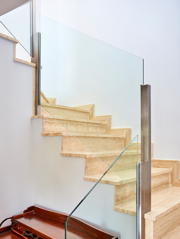 Modern u-shaped glass railing staircase in Madrid with marble treads and marble risers.