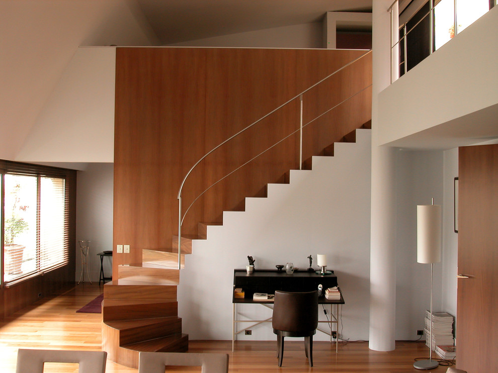 This is an example of a large modern wood curved staircase in Paris with wood risers and feature lighting.
