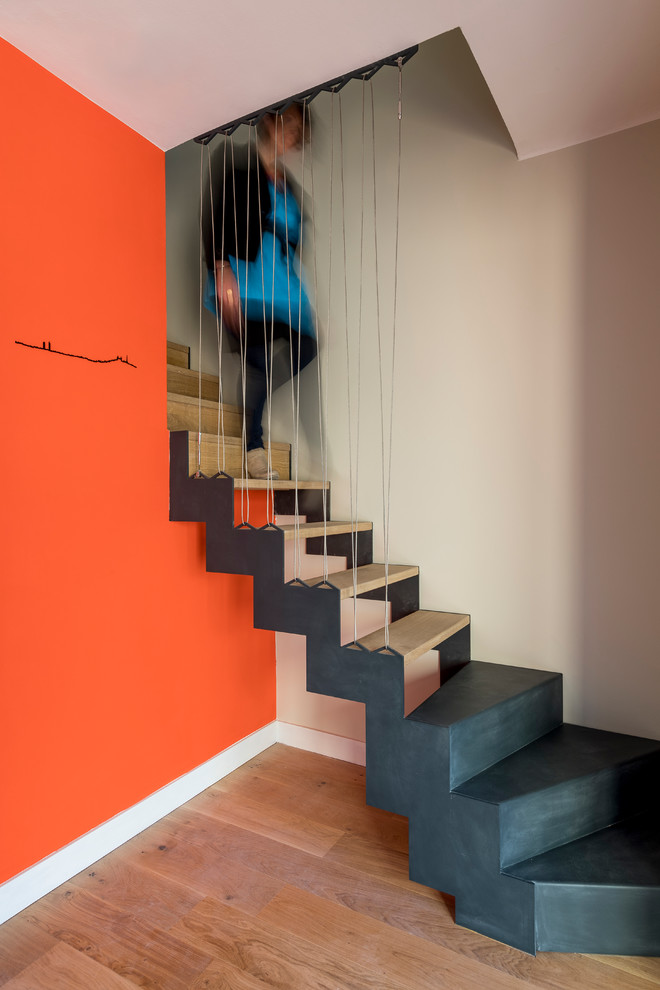 Aménagement d'un grand escalier courbe contemporain avec des marches en bois, des contremarches en bois et un garde-corps en câble.