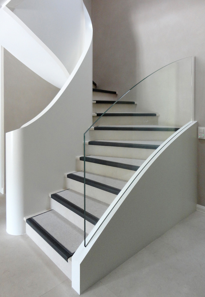Стильный дизайн: изогнутая лестница в стиле кантри с ступенями из известняка, подступенками из известняка и стеклянными перилами - последний тренд