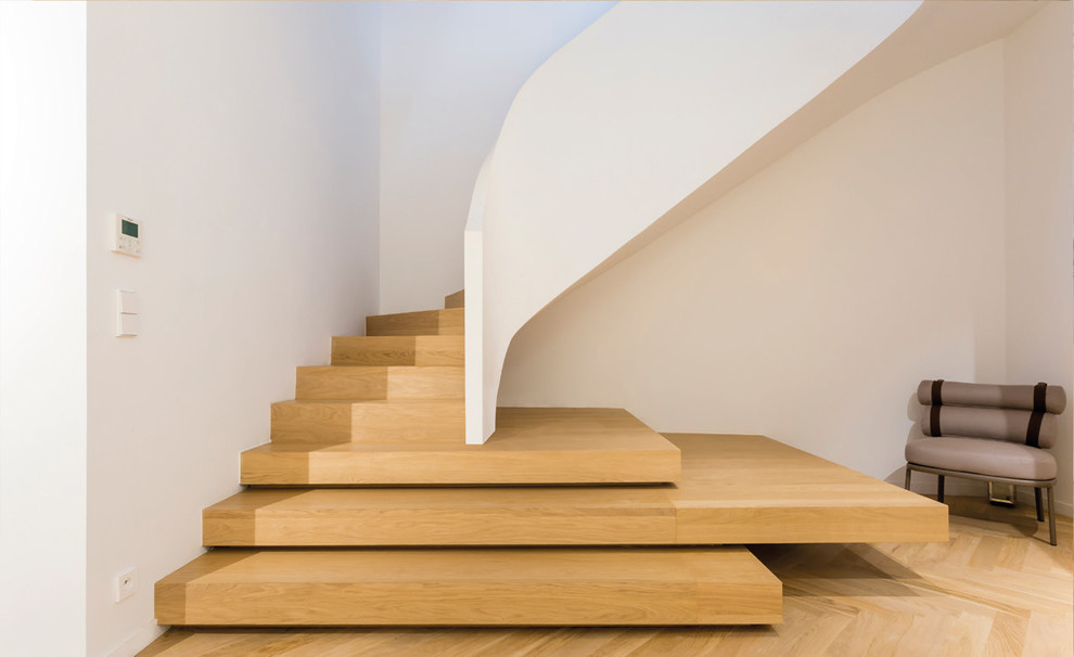 Immagine di una scala curva minimalista con pedata in legno, alzata in legno e parapetto in materiali misti