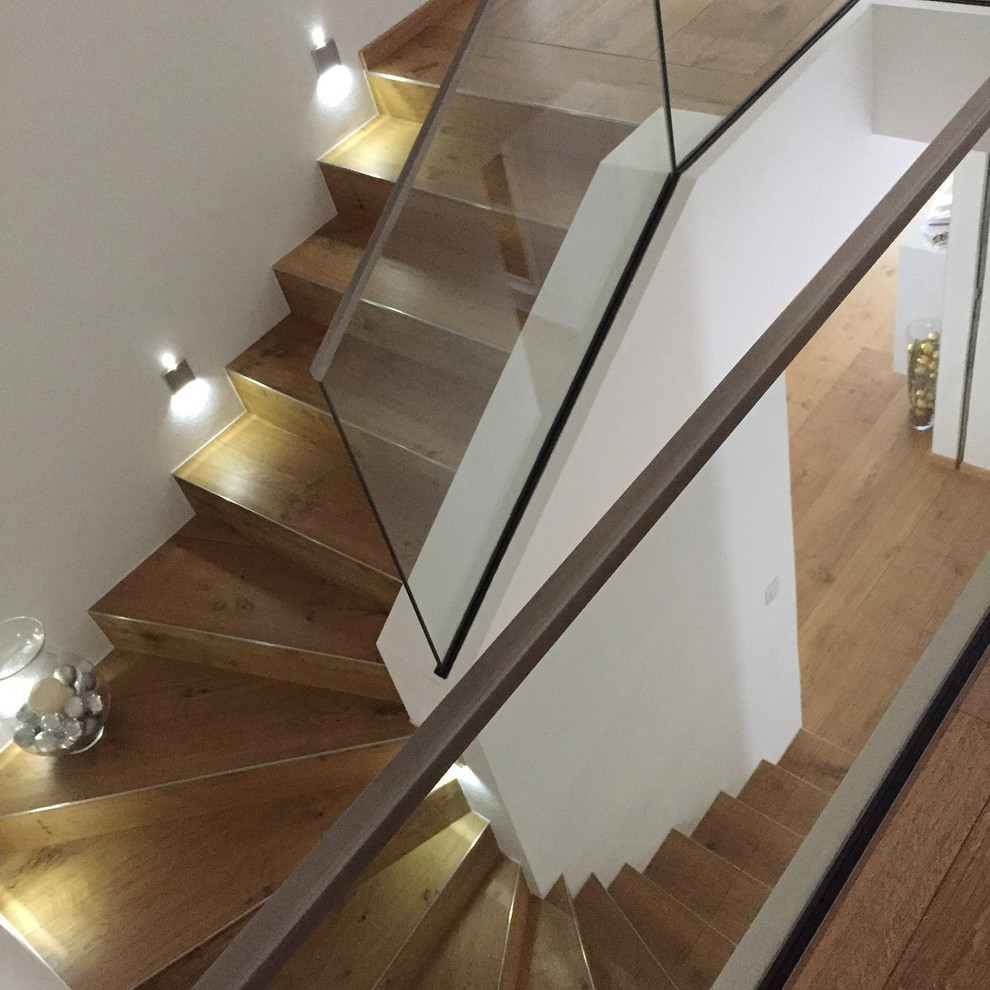 Cette image montre un escalier design en U de taille moyenne avec des marches en bois, des contremarches en verre et un garde-corps en verre.