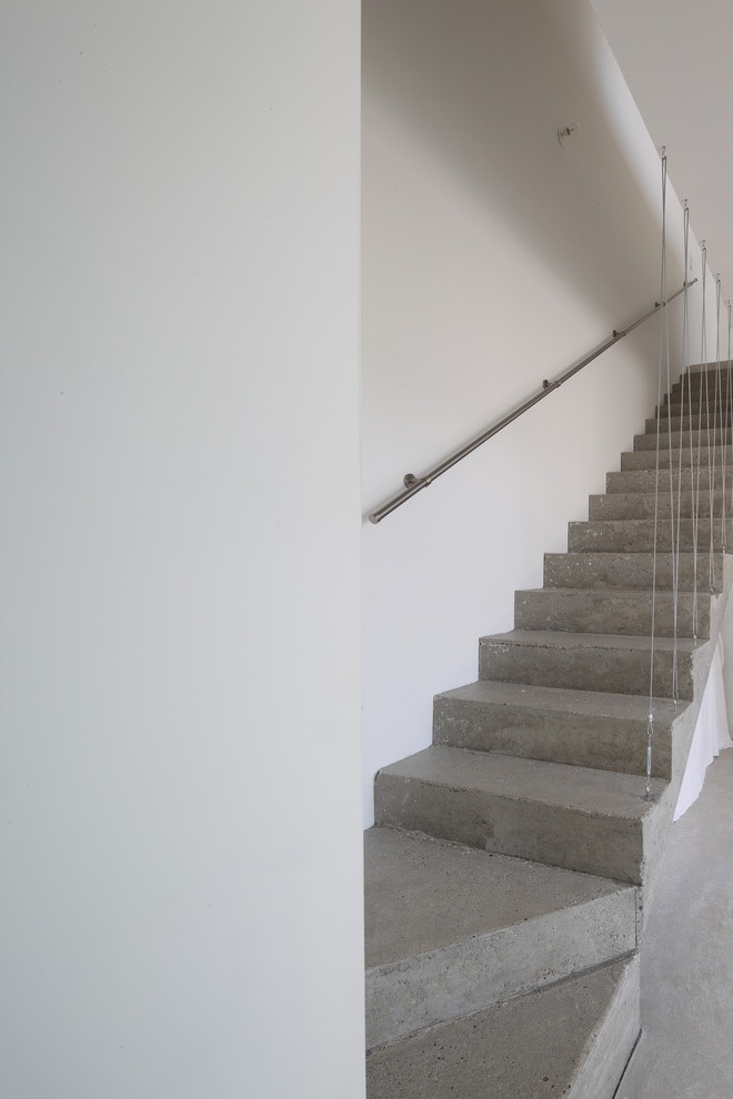 На фото: изогнутая бетонная лестница в современном стиле с бетонными ступенями и перилами из тросов с