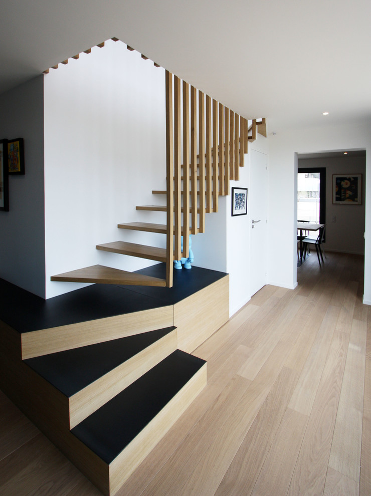 Exempel på en stor modern svängd trappa i trä, med öppna sättsteg och räcke i trä