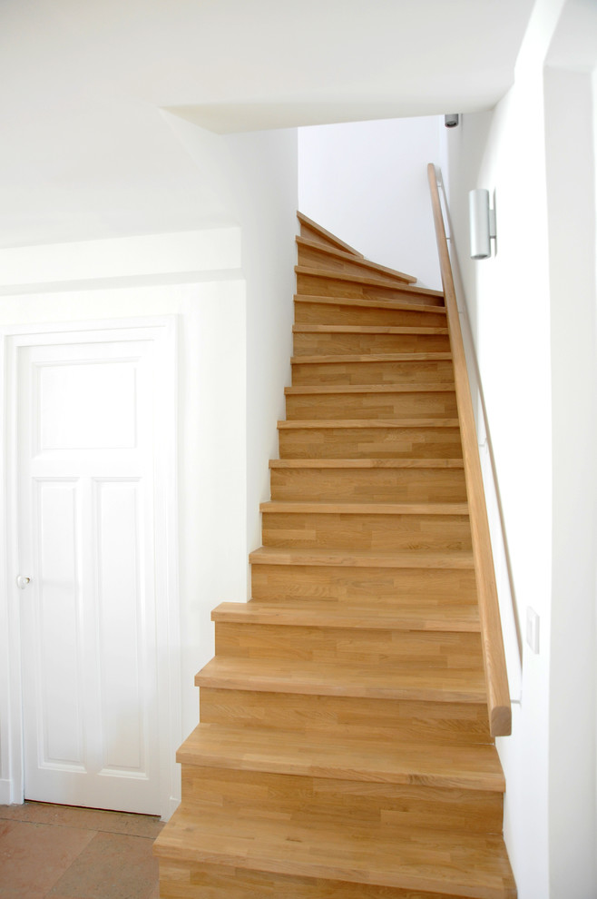 На фото: большая изогнутая деревянная лестница в классическом стиле с деревянными ступенями