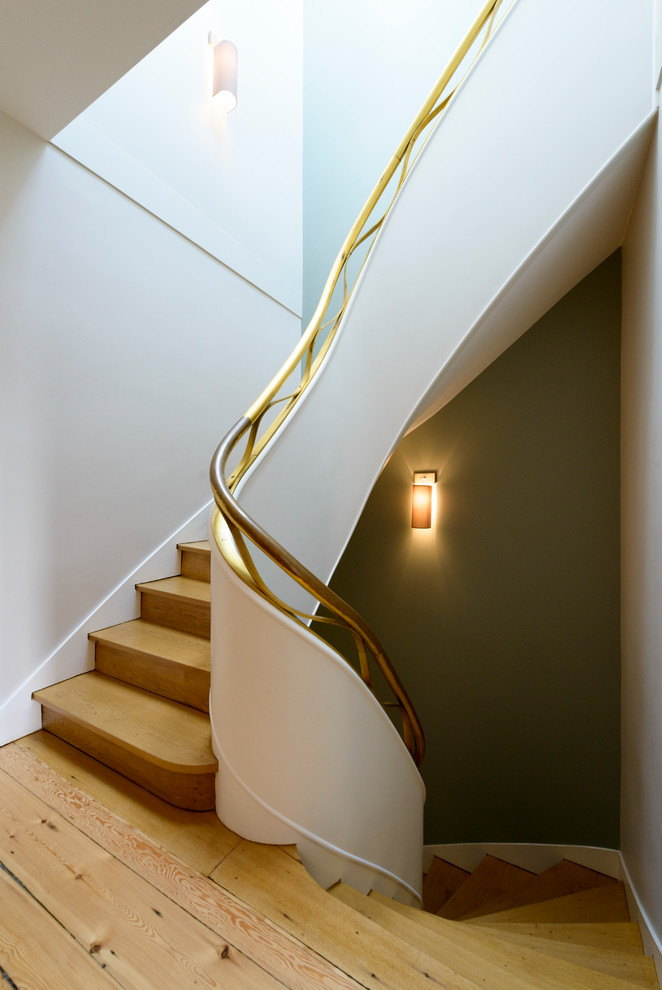 На фото: изогнутая деревянная лестница в стиле неоклассика (современная классика) с деревянными ступенями и металлическими перилами с