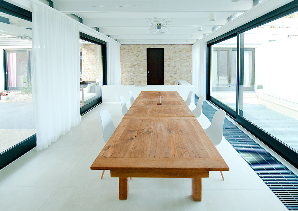 Foto di una grande sala da pranzo aperta verso il soggiorno minimal con pareti bianche, pavimento in gres porcellanato, camino classico e cornice del camino piastrellata