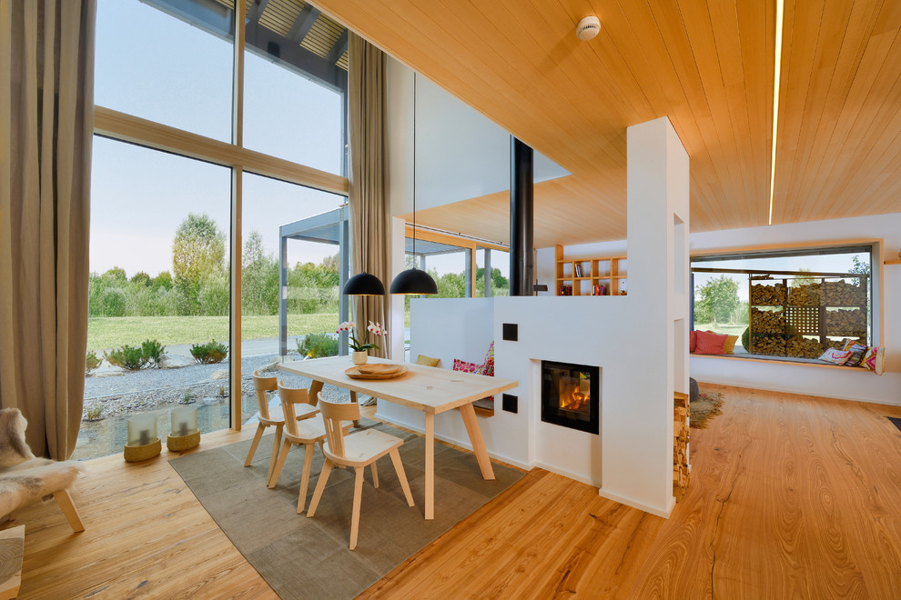 Aménagement d'une grande salle à manger scandinave avec un mur blanc, une cheminée double-face, un sol en bois brun et un manteau de cheminée en métal.