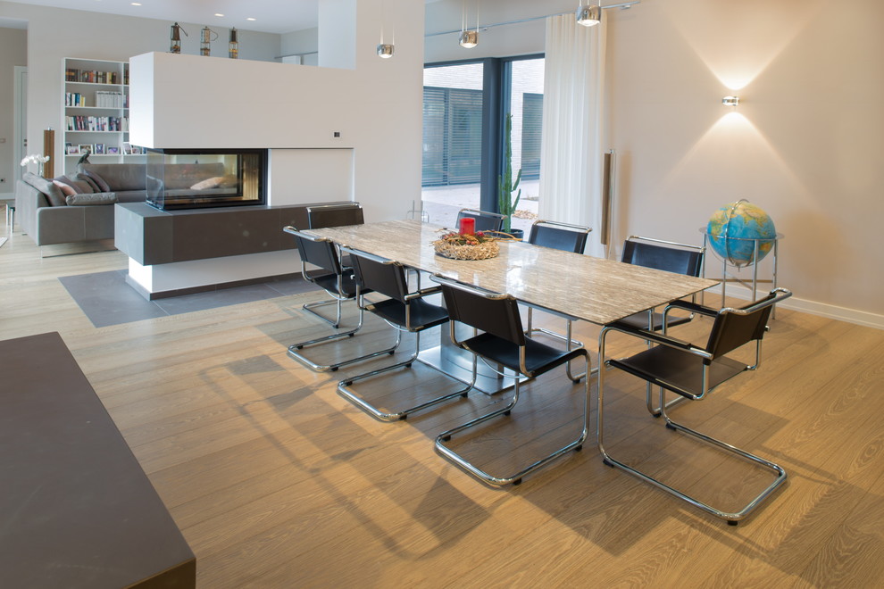 Immagine di un'ampia sala da pranzo aperta verso la cucina minimal con pareti marroni, pavimento in legno massello medio, stufa a legna, cornice del camino in mattoni e pavimento marrone