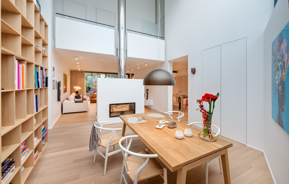 Example of a huge trendy light wood floor and brown floor great room design in Cologne with white walls, a two-sided fireplace and a plaster fireplace