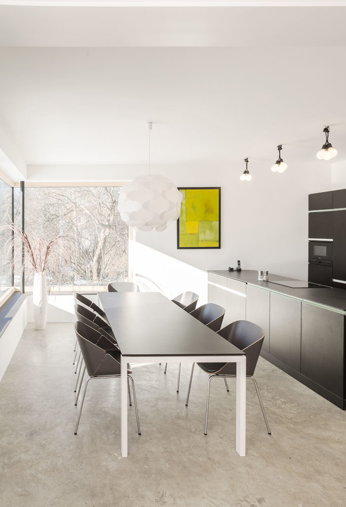 Cette image montre une salle à manger ouverte sur la cuisine minimaliste de taille moyenne avec un mur blanc, sol en béton ciré, un sol gris et aucune cheminée.