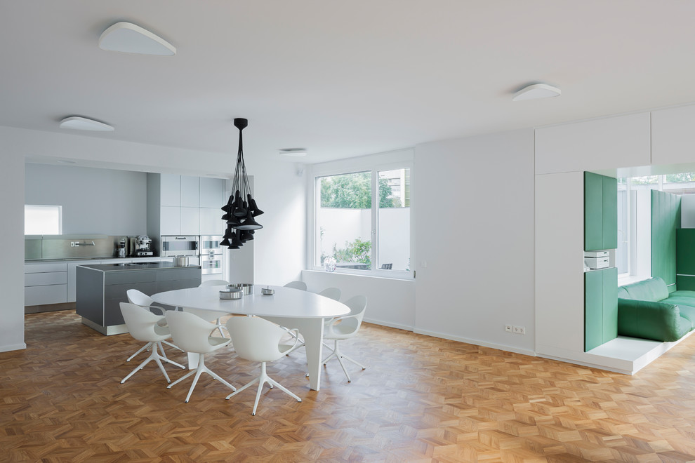 Modelo de comedor contemporáneo grande abierto sin chimenea con paredes blancas, suelo de madera en tonos medios y suelo marrón