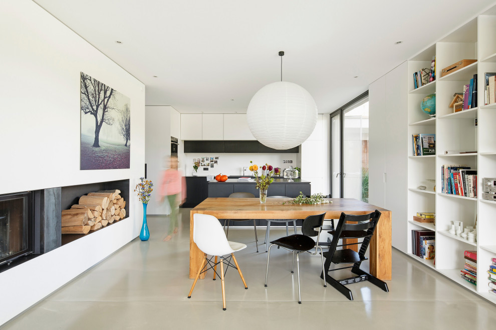 Modelo de comedor minimalista abierto con paredes blancas, suelo de cemento, todas las chimeneas y suelo gris