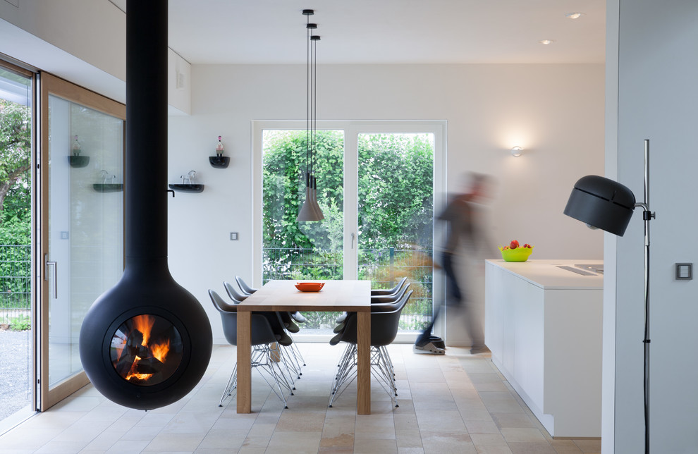 Cette image montre une salle à manger ouverte sur la cuisine design de taille moyenne avec un mur blanc, un sol en travertin, cheminée suspendue, un manteau de cheminée en métal et éclairage.