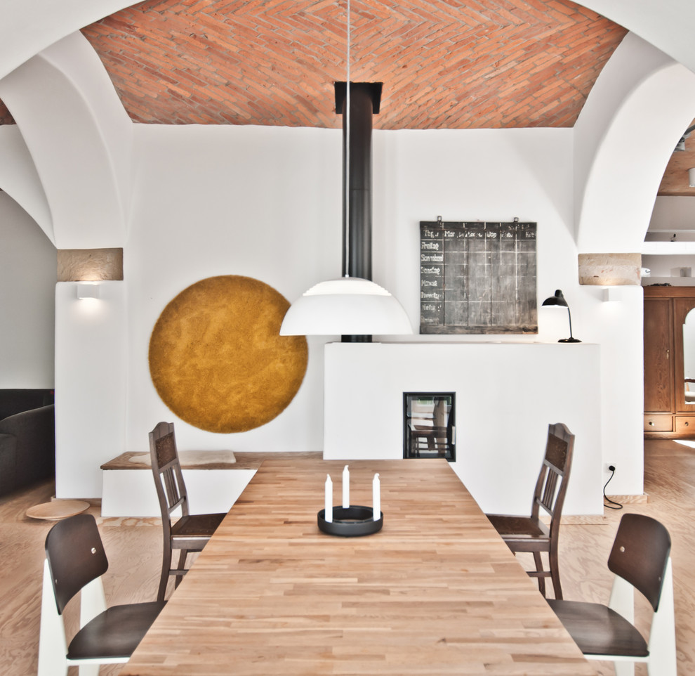 Пример оригинального дизайна: гостиная-столовая среднего размера в скандинавском стиле с белыми стенами, фасадом камина из штукатурки, коричневым полом, светлым паркетным полом и печью-буржуйкой