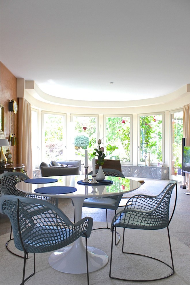 Пример оригинального дизайна: большая гостиная-столовая в стиле фьюжн с оранжевыми стенами, ковровым покрытием, угловым камином, фасадом камина из бетона и серым полом