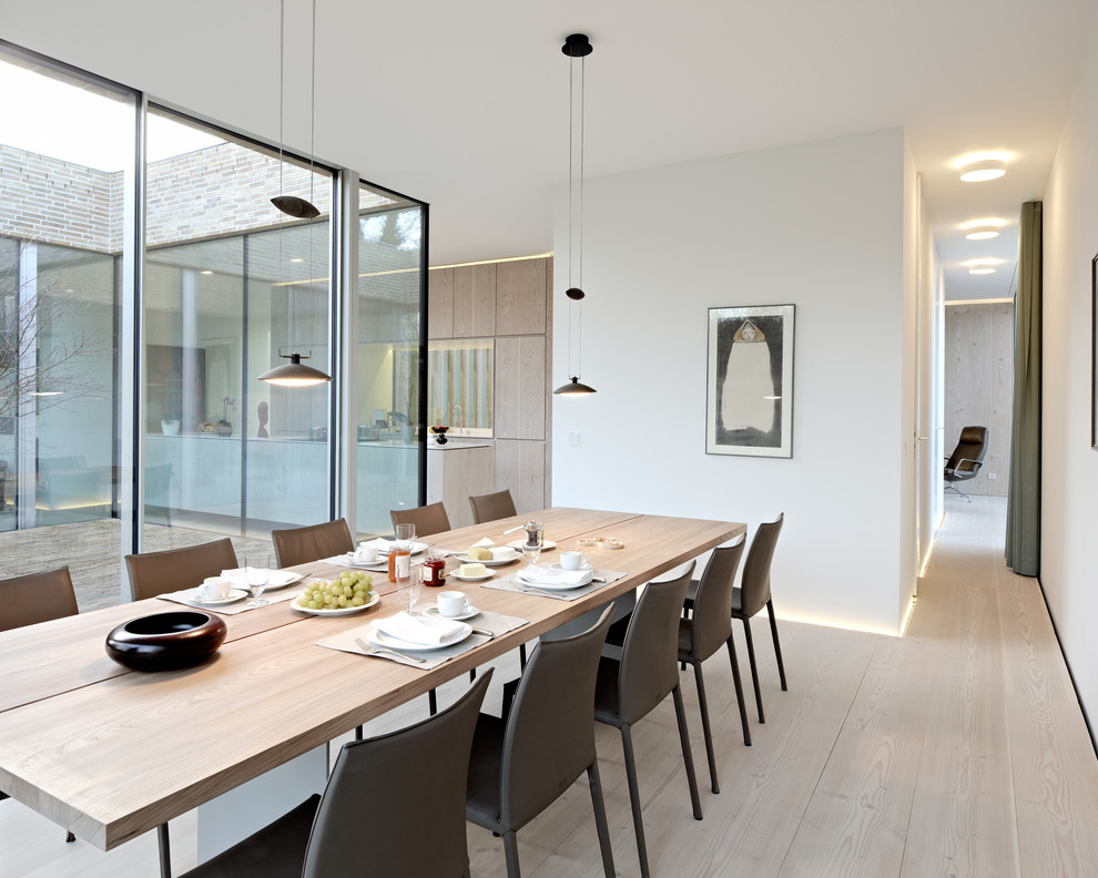 Large contemporary open plan dining room in Hamburg with light hardwood flooring, white walls and feature lighting.