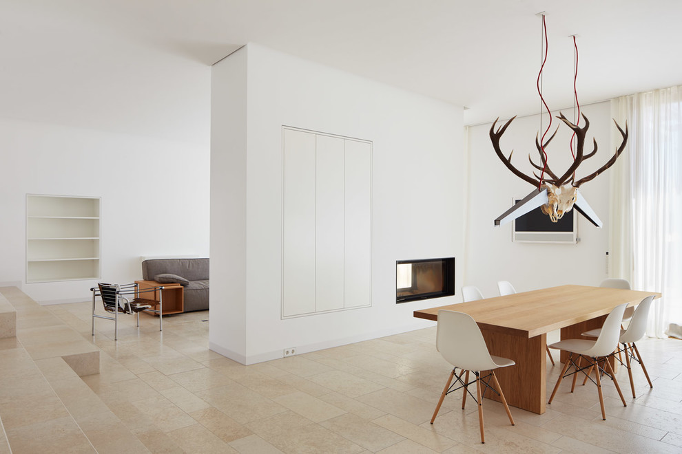 Идея дизайна: гостиная-столовая среднего размера в скандинавском стиле с белыми стенами, полом из травертина, двусторонним камином, фасадом камина из штукатурки и бежевым полом