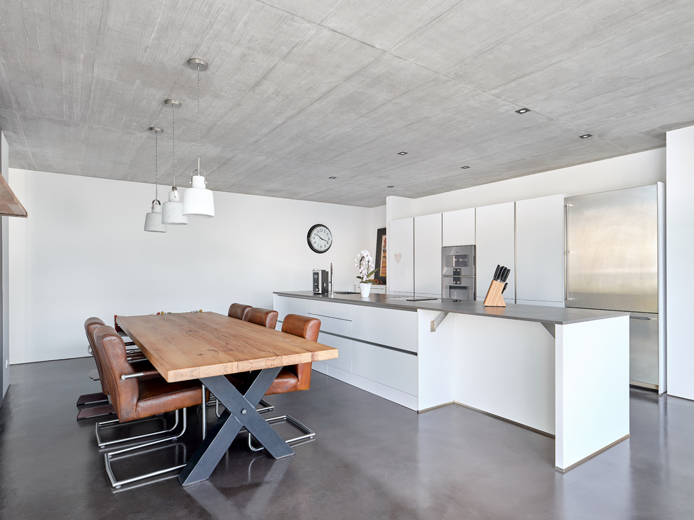 Foto di una sala da pranzo aperta verso la cucina design con pareti bianche, pavimento in cemento e pavimento grigio