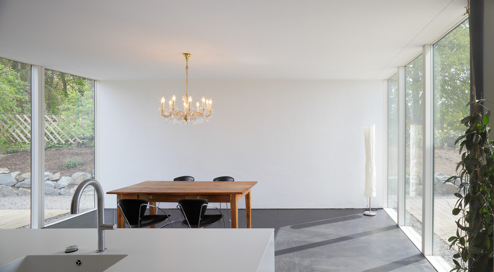 Foto di una sala da pranzo aperta verso la cucina contemporanea di medie dimensioni con pareti bianche e pavimento in cemento