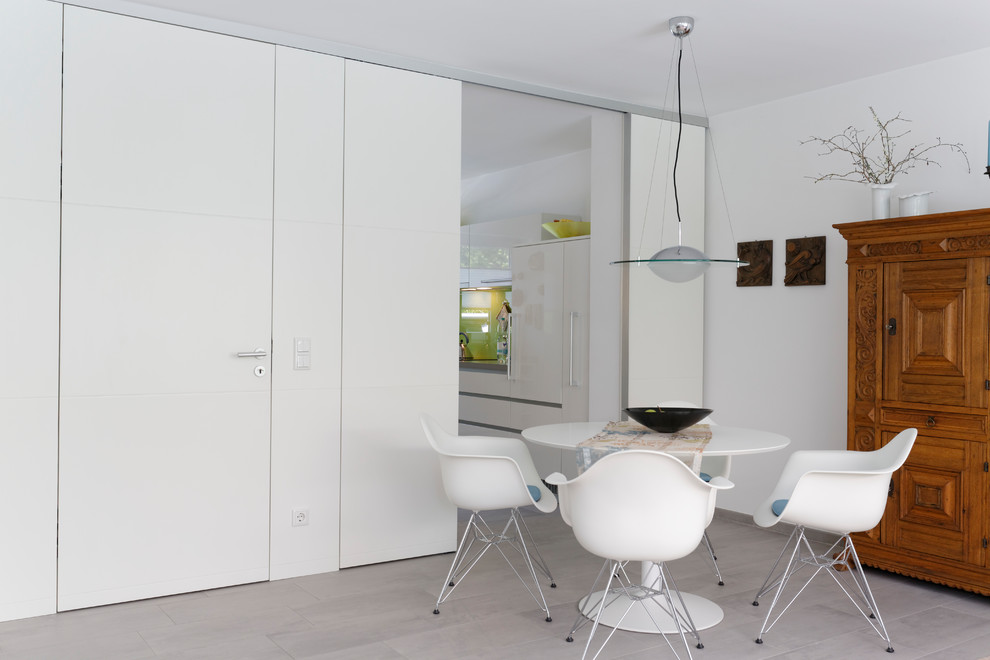Cette image montre une salle à manger ouverte sur le salon design avec un mur blanc, un sol en carrelage de céramique et un sol gris.