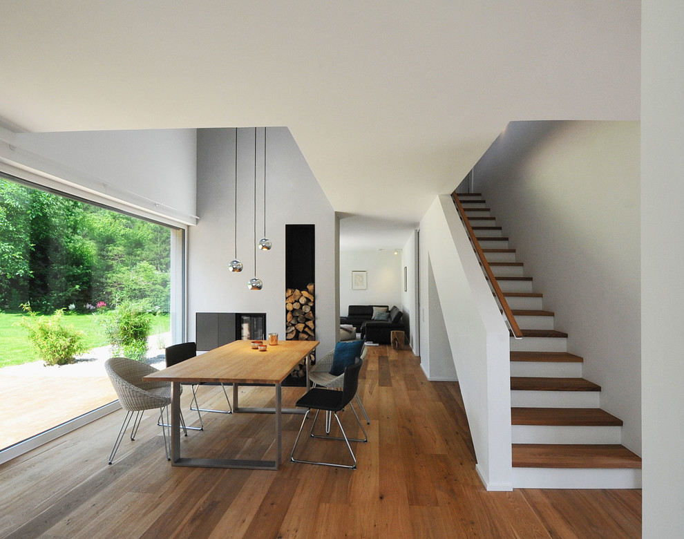 Cette image montre une salle à manger ouverte sur le salon design de taille moyenne avec un mur gris, un sol en bois brun, une cheminée double-face, un manteau de cheminée en métal et un sol marron.