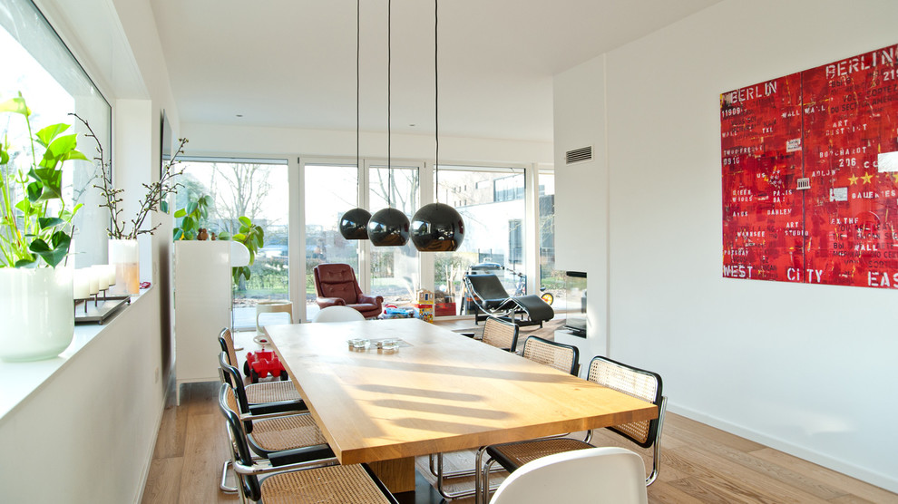 Esempio di una sala da pranzo aperta verso il soggiorno design di medie dimensioni con pareti bianche, parquet chiaro e cornice del camino in intonaco