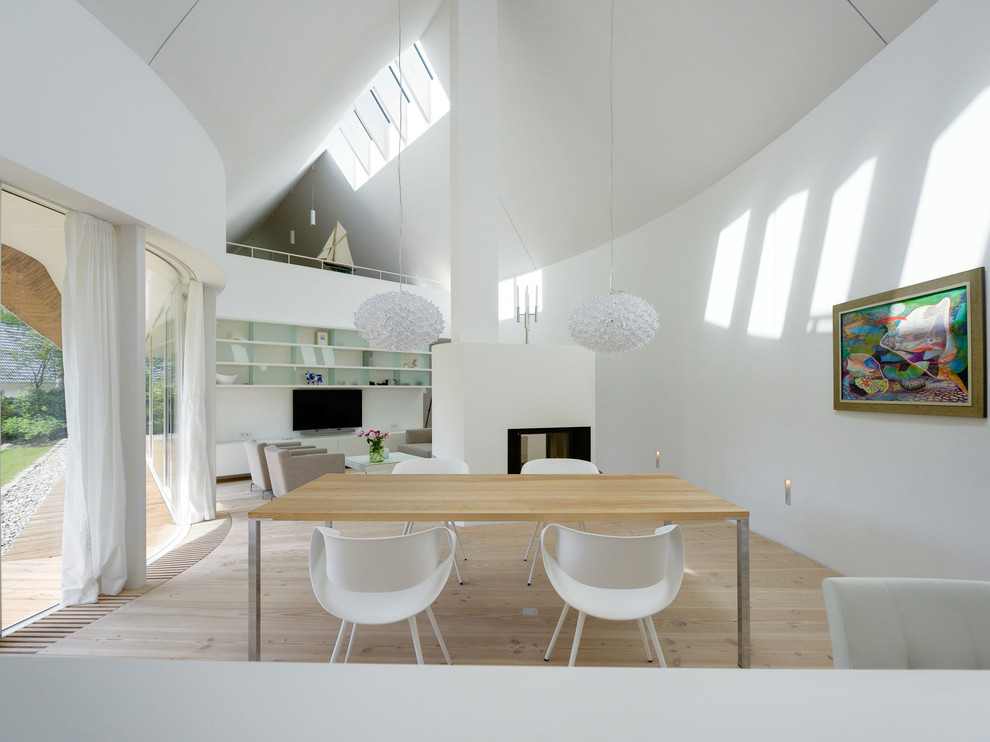 На фото: большая гостиная-столовая в современном стиле с белыми стенами и двусторонним камином с