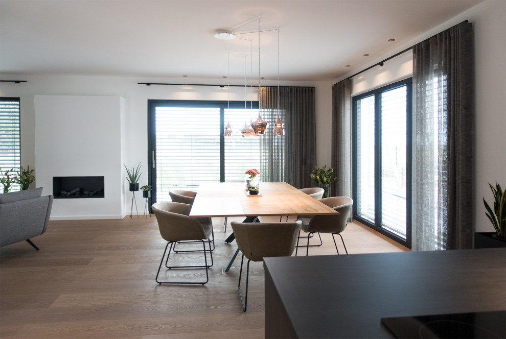 Immagine di un'ampia sala da pranzo aperta verso il soggiorno contemporanea con pareti bianche, pavimento in laminato e pavimento marrone