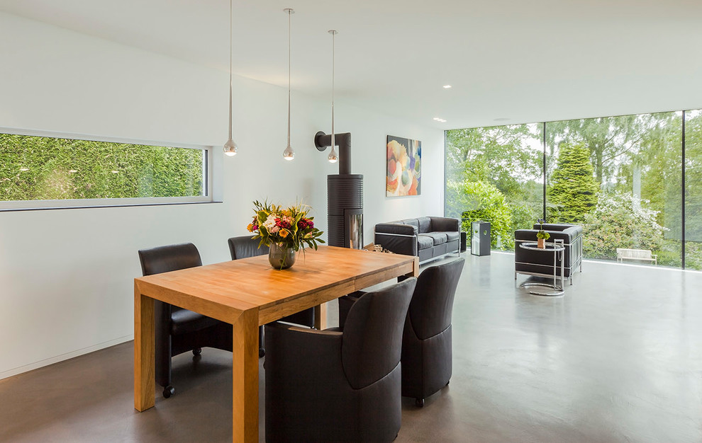 Immagine di una sala da pranzo aperta verso il soggiorno moderna di medie dimensioni con pareti bianche, pavimento in cemento, stufa a legna, cornice del camino in metallo e pavimento grigio