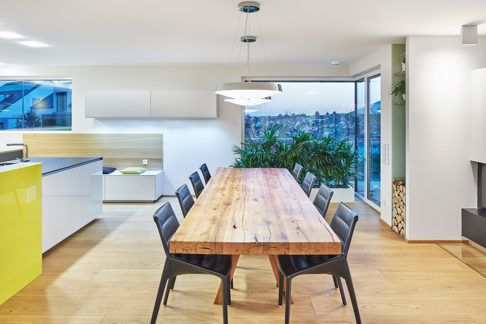 Inspiration pour une salle à manger ouverte sur le salon minimaliste de taille moyenne avec un mur gris, un sol en bois brun, une cheminée d'angle, un manteau de cheminée en plâtre et un sol beige.