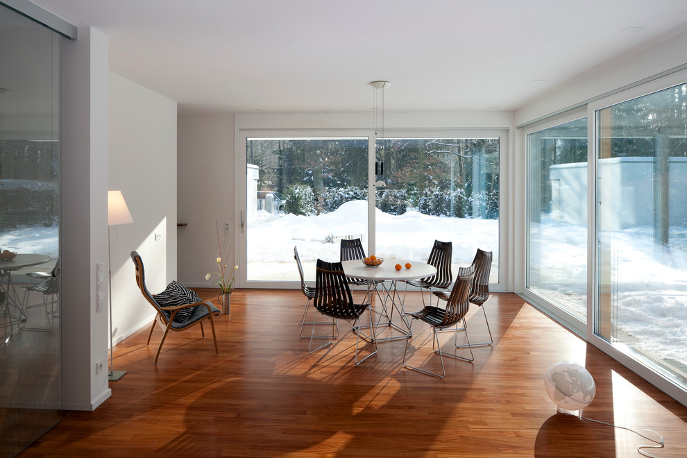 Imagen de comedor contemporáneo cerrado con paredes blancas y suelo de madera en tonos medios