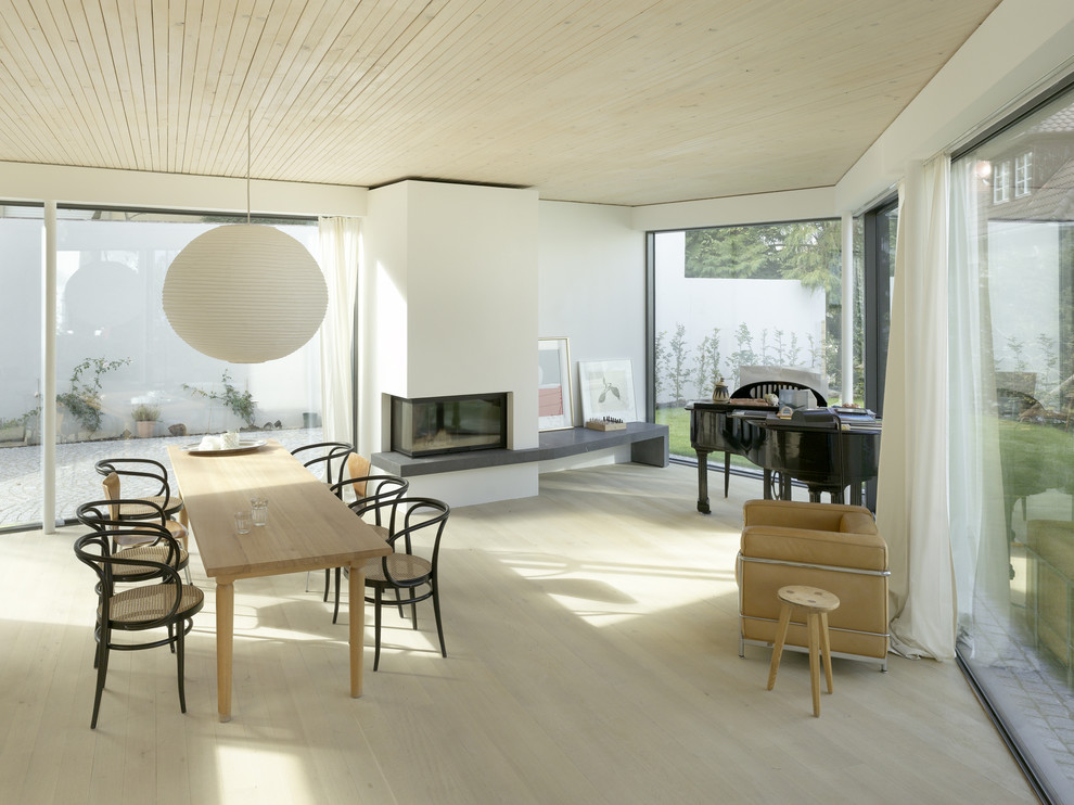 Foto di una sala da pranzo aperta verso il soggiorno minimal con pareti bianche, parquet chiaro e camino classico