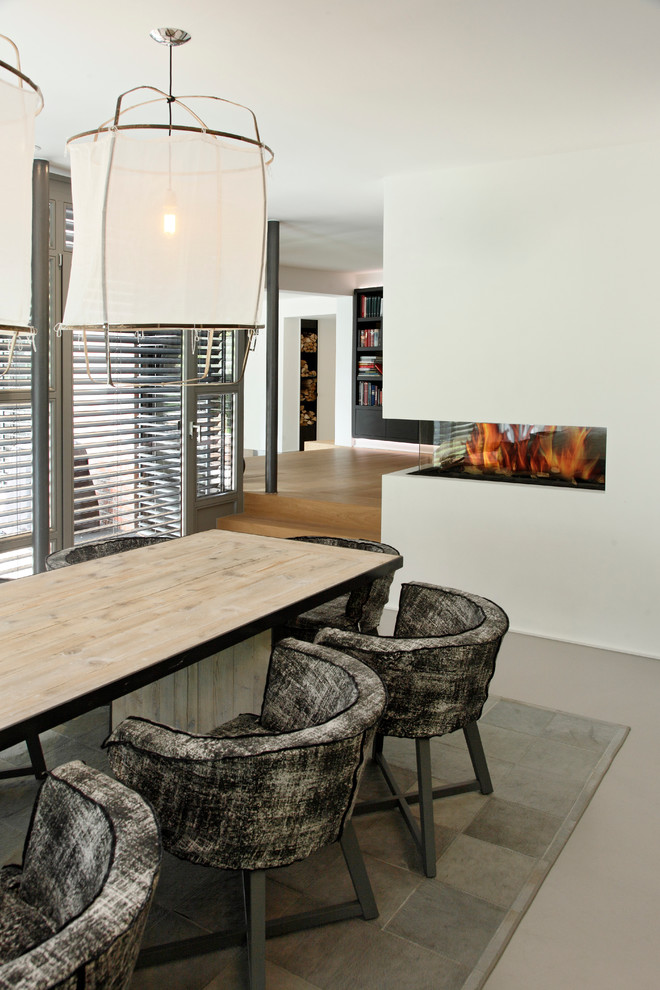 Idée de décoration pour une salle à manger ouverte sur le salon minimaliste avec un mur blanc, une cheminée double-face et un manteau de cheminée en plâtre.