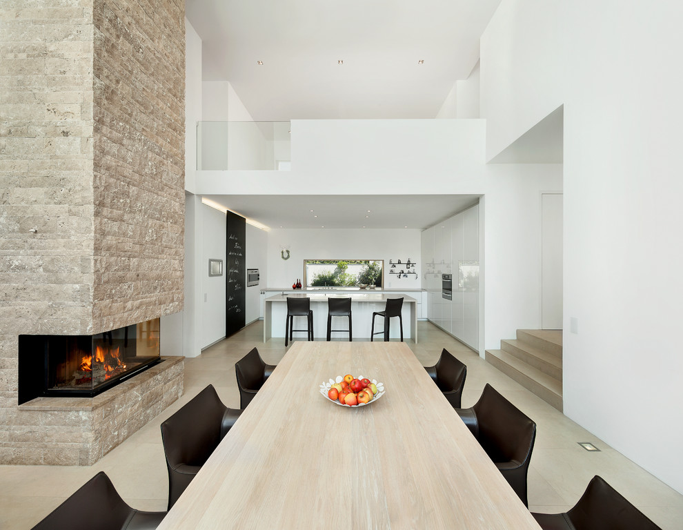 Стильный дизайн: большая кухня-столовая в стиле модернизм с белыми стенами, светлым паркетным полом, двусторонним камином и фасадом камина из камня - последний тренд
