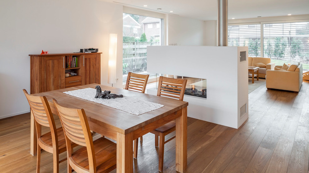 Aménagement d'une salle à manger ouverte sur le salon scandinave de taille moyenne avec un mur blanc, une cheminée double-face, un manteau de cheminée en plâtre, un sol marron et un sol en bois brun.
