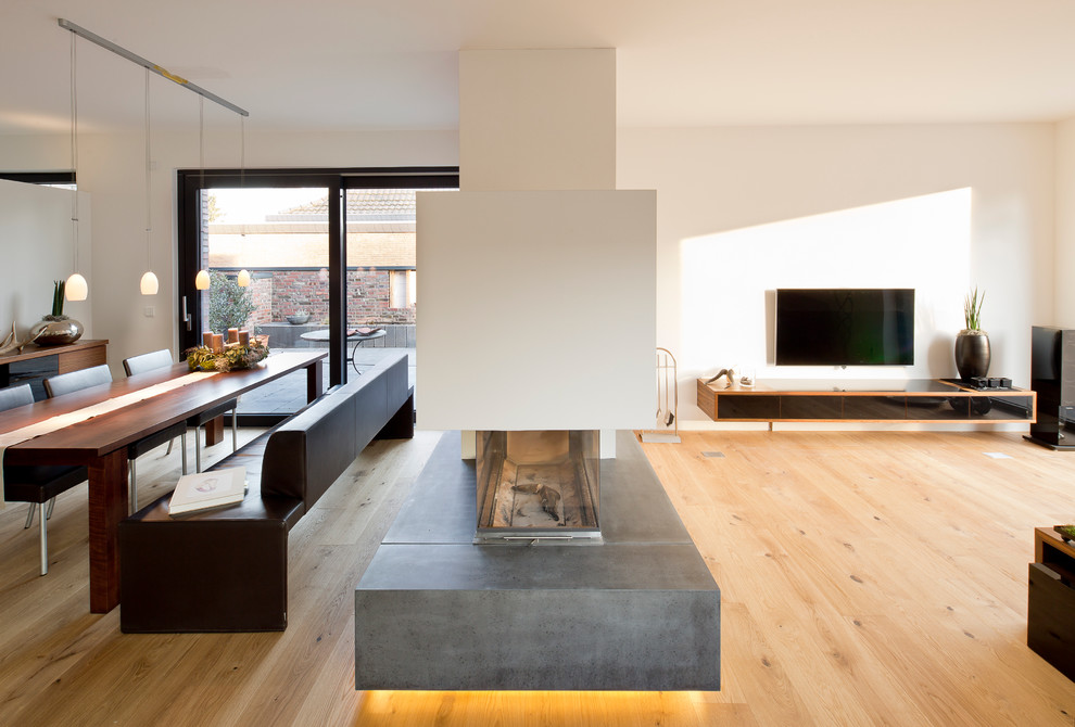 Ejemplo de comedor contemporáneo, grande, abierto, con paredes blancas, suelo de madera clara, chimenea de doble cara y marco de chimenea de yeso